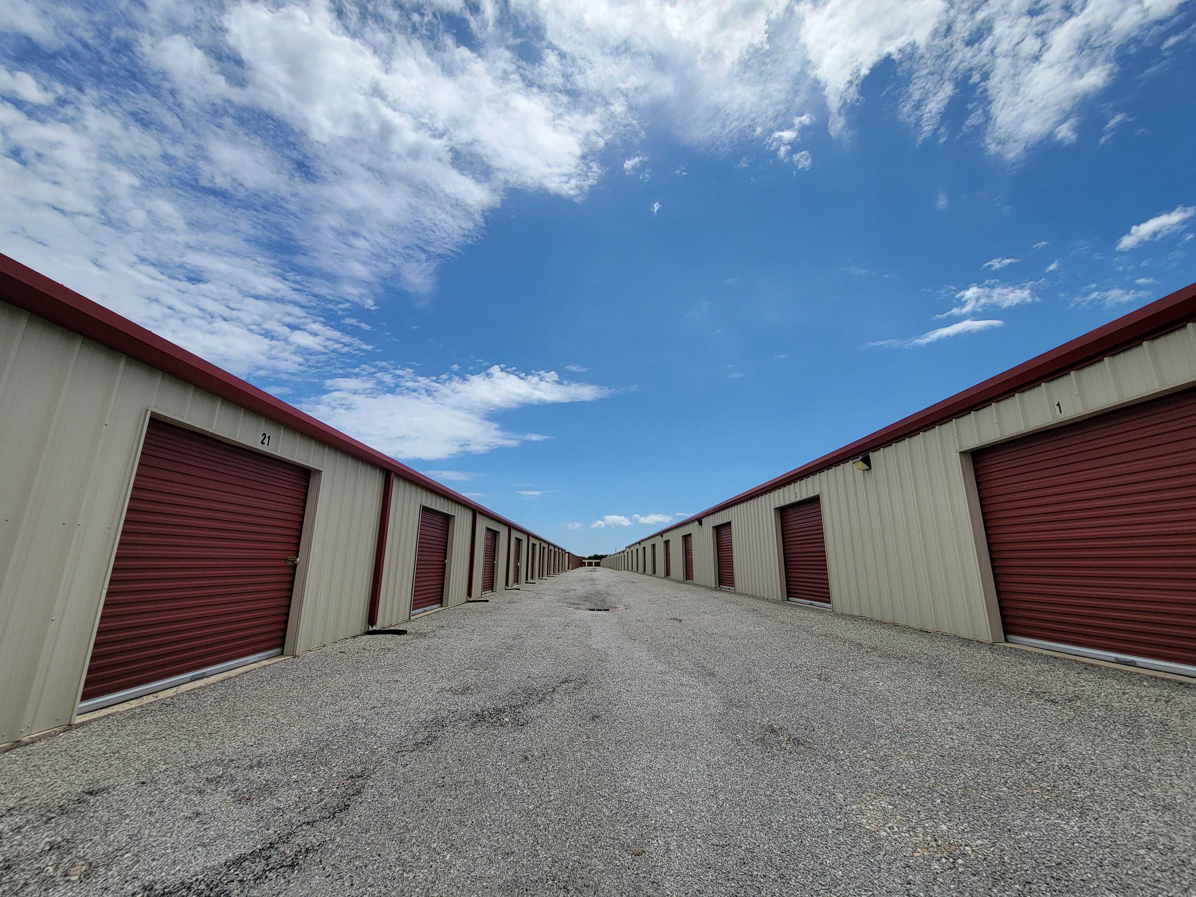 Outdoor drive-up storage units with red roll-up doors at Caddo Mills Climate Storage under a blue Texas sky